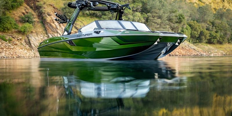 Green motorboat with black trim floating on calm water near a rocky, tree-covered shoreline.