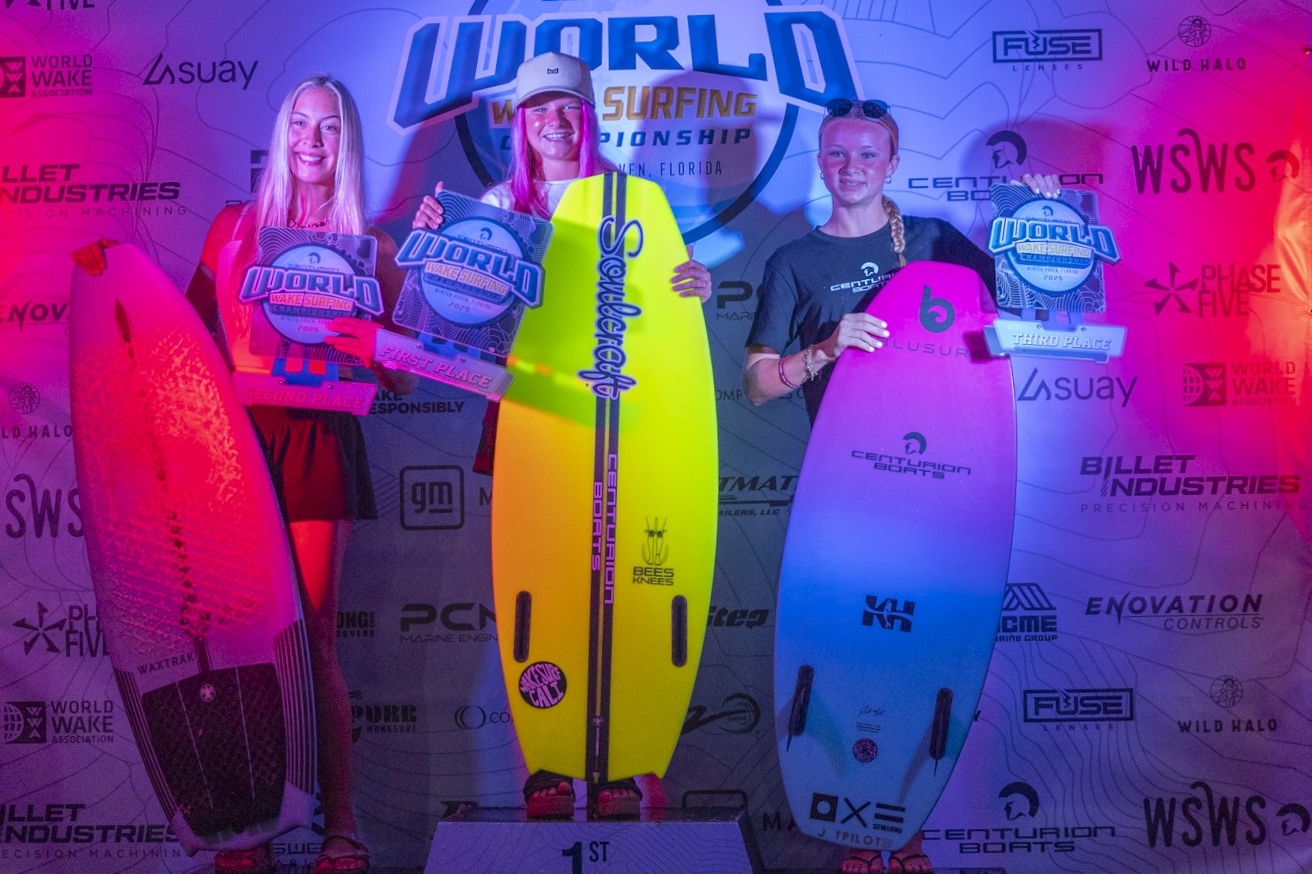 Three surfers stand on a podium holding surfboards and plaques for 1st, 2nd, and 3rd place at the Centurion World Surfing Championship, with a branded backdrop behind them.