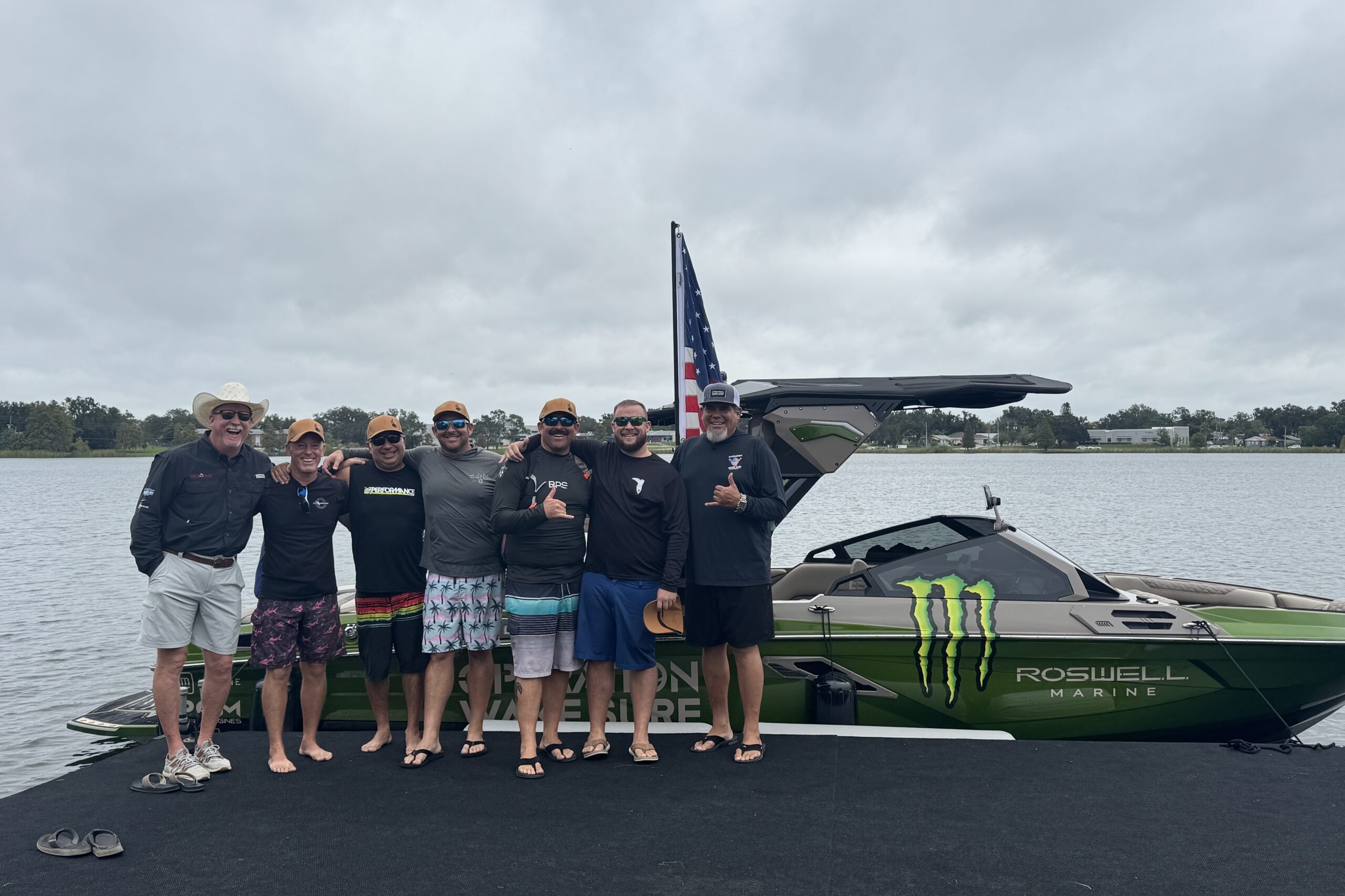 Seven men stand together on a dock in front of a green Roswell Marine boat with Monster Energy branding, smiling and posing for a group photo.
