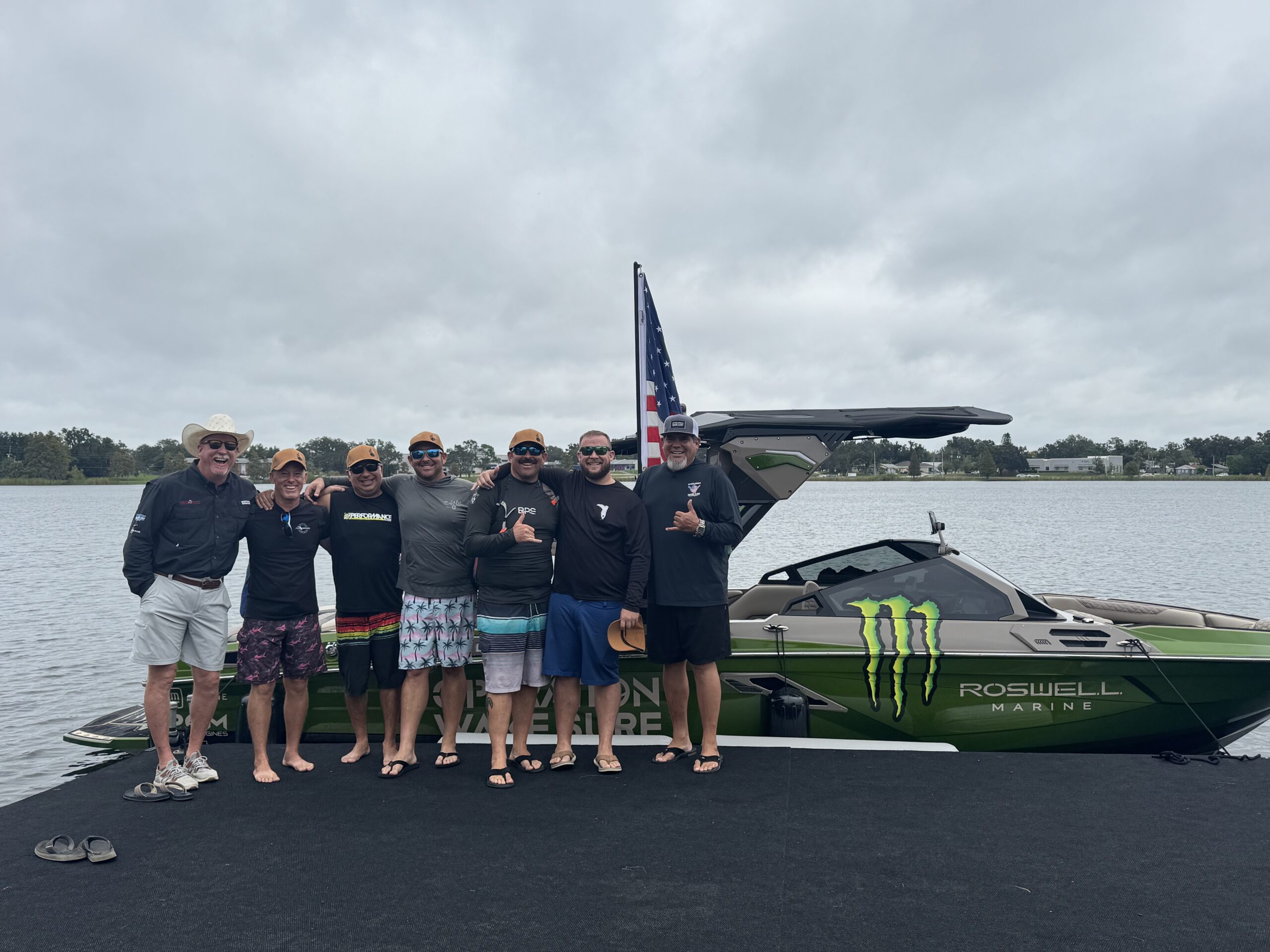 Seven men stand together on a dock in front of a green Roswell Marine boat with Monster Energy branding, smiling and posing for a group photo.