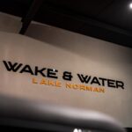 A wall sign reads "Wake & Water Lake Norman" in black and orange letters against a white background.