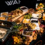 A buffet table with assorted cheeses, crackers, fruit, vegetables, cold cuts, olives, and bread, arranged on platters and trays for a gathering or event.