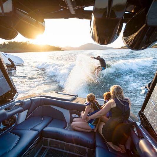 Clair Hurta wakeboards behind a boat at sunset while three people sit and watch from inside the boat.