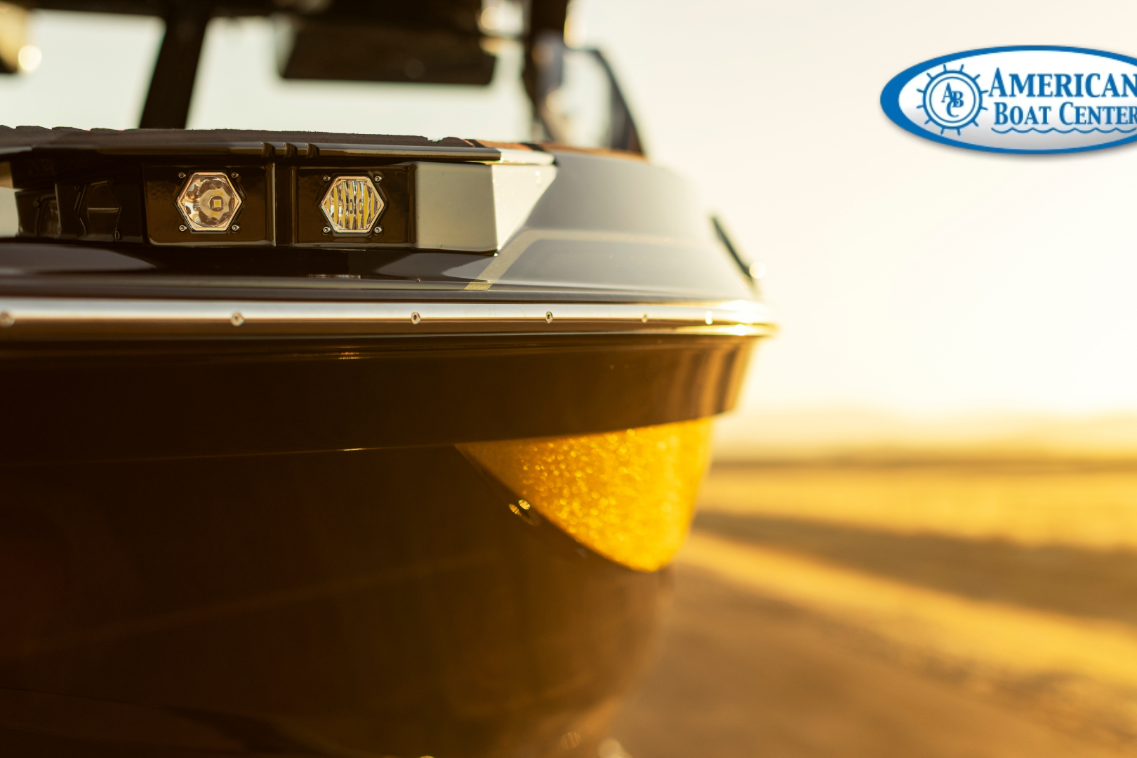 Close-up of the front side of a black boat in sunlight, with the American Boat Center logo in the upper right corner.