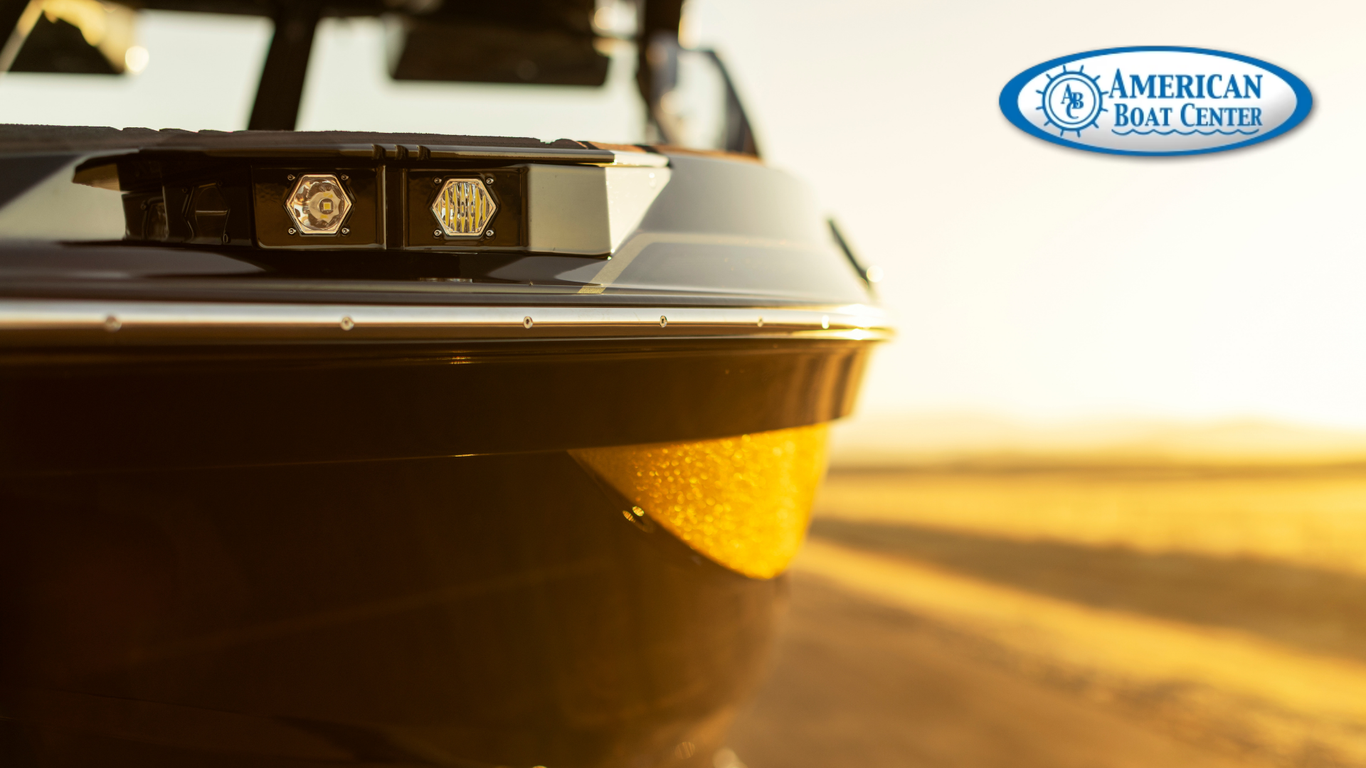 Close-up of the front side of a black boat in sunlight, with the American Boat Center logo in the upper right corner.