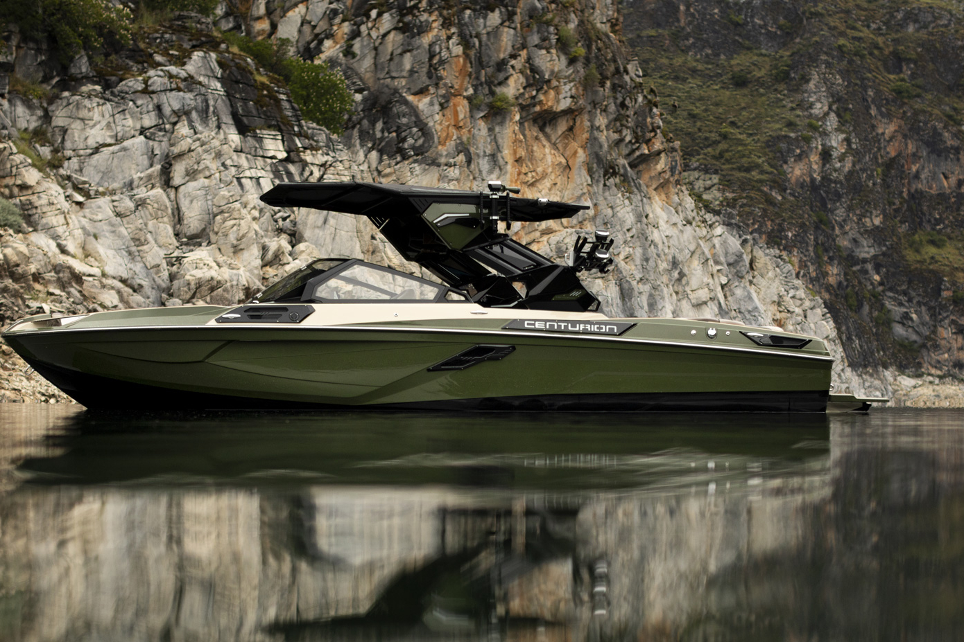 A green Centurion speedboat is floating on calm water near rocky cliffs with greenery in the background.