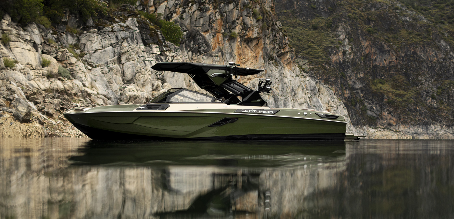 A green Centurion speedboat is floating on calm water near rocky cliffs with greenery in the background.